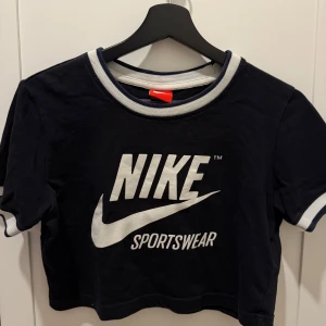 Svart croppad Nike t-shirt S - Svart croppad t-shirt från Nike med vit logga och texten 'Sportswear' på bröstet. Modellen är kortärmad och gjord i mjuk bomull, perfekt för en sportig och chill stil.
