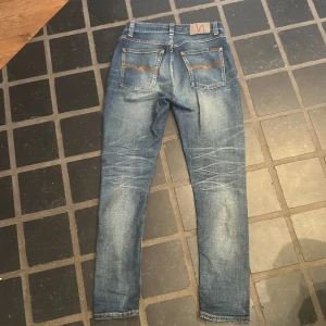Blå Nudie Jeans Co jeans W24 L28 - Snygga blå jeans från Nudie Jeans Co med klassisk orange söm och vågig brodyr på bakfickorna. Modellen är slim fit. Passar mellan 160-170cm lång. Inga fel och är i bra skick 