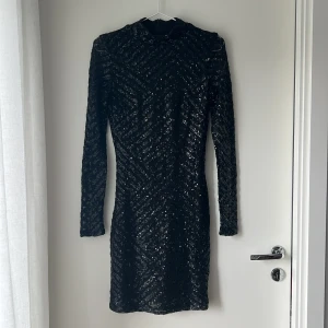 Svart paljettklänning Gina Tricot S - Supersnygg svart kort paljettklänning från Gina Tricot i storlek S. Klänningen har långa ärmar, rund hals och är täckt av glittriga paljetter i ett mönster som ger en riktigt festlig vibe. Perfekt för dig som vill sticka ut och glänsa.