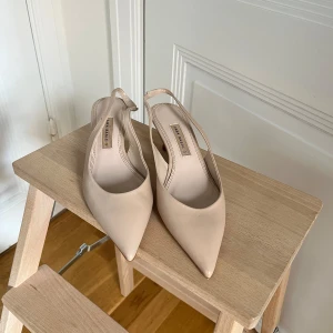 Beige pumps spetsig tå från Zara strl 37 - Snygga beige pumps från Zara i äkta skinn med spetsig tå och låg klack. Skorna har öppen häl med rem. Nya utan prislapp. 