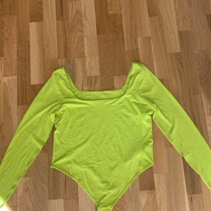 Lululemon Limegrön långärmad bodysuit  - Supermjuk och stretchig limegrön bodysuit från Lululemon med fyrkantig ringning och stringskärning. Långärmad modell i deras Nulu-material som är lätt, snabbtorkande och följsam. Perfekt för dig som vill ha en snygg och bekväm topp med tight passform och modern vibe. Den finns en liten fläck som kanske går att få bort. Lappen sitter kvar och den har aldrig använts, jag säljer pga att den inte passar. Nypris:940 kr. 