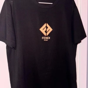 Svart Diamond print Fendi t-shirt - Svart t-shirt från Fendi med ikonisk guldfärgad logga och texten 'Fendi Roma' på bröstet. Klassisk passform med rund hals och korta ärmar. Materialet känns mjukt och skönt, perfekt för en stilren och trendig look.