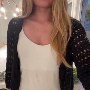 Bolero  - Svart kofta med lång ärm, virkad i ett snyggt hålmönster. Koftan är öppen framtill och har en loose passform, perfekt att slänga över en topp. Materialet känns stickat och ger en chill vibe till outfiten.