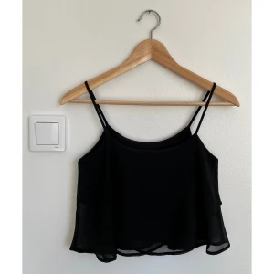 Svart croppad topp från Bershka - Svart croppad topp från Bershka med tunna axelband och dubbla lager i lätt, transparent polyester. Toppen har en flowy passform och är perfekt för dig som gillar minimalistisk stil med en touch av edge. Snygg att matcha med jeans eller kjol.