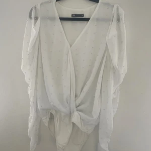Vit omlottblus med pärlor från Zara - Supersnygg vit omlottblus från Zara med pärldetaljer över hela tyget. Blusen har v-ringning, långa puffiga ärmar och är gjord i ett tunt, flowy material. Perfekt för dig som vill sticka ut med en elegant och trendig look.