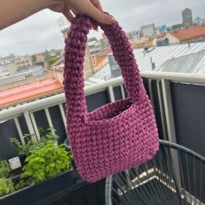 Virkad väska - Hemmavirkad lila väska i 100% t-shirtgarn i överskott från textilindustrin. Väskan är 23cm bred, 16cm hög och 36cm hög inklusive handtag. Aldrig använd