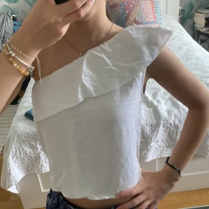 Volang topp  - Superfin vit one shoulder topp från Brownie i linne. Toppen har en bred volang längs halsringningen som ger en snygg och trendig look. Perfekt till sommaren och passar till både jeans och kjol. Säljer då den inte kommer till användning längre! Står xss men skulle säga att den passar mer xs