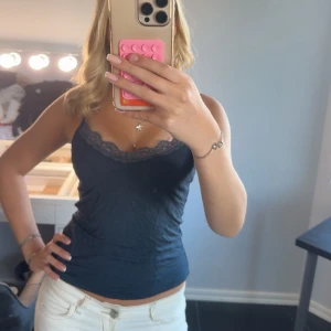 Marinblått linne med spets - Snygg mörkblå linnetopp med tunna axelband och dekorativ längs urringningen. Toppen är figurnära och har en enkel, stilren look som passar perfekt till jeans.