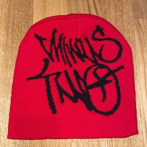 Röd mössa med svart graffiti-tryck - Cool röd mössa med svart graffiti-inspirerad text framtill. Mössan är slätstickad och har en klassisk, enkel form utan tofs eller vik. Perfekt för dig som vill sticka ut med streetstyle-vibe. Materialet känns mjukt och stretchigt, troligen i bomull eller syntet.
