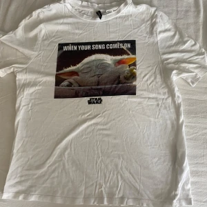 Vit Star Wars t-shirt från H&M Divided - Vit t-shirt från H&M Divided med tryck av Baby Yoda och texten 'When your song comes on'. korta ärmar. Perfekt för dig som älskar Star Wars och vill ha en chill och rolig look.