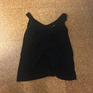 Svart linnetopp från H&M XS - Svart linnetopp från H&M i storlek XS. Toppen har breda axelband och en snygg v-ringning med vävt band upptill som ger en cool detalj. Perfekt att styla med jeans eller kjol för en enkel men stilren look.