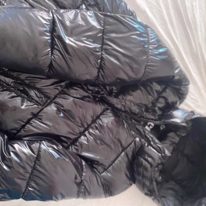 Svart pufferjacka från ONLY Premium - Säljer en glansig svart pufferjacka från ONLY Premium i storlek S. Jackan har quiltad design och dragkedja framtill. Perfekt för kalla dagar när du vill hålla stilen och värmen. Snygg och trendig look som passar till det mesta.