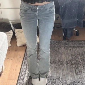 Grå bootcut jeans från Gina Tricot - Snygga grå jeans från Gina Tricot i bootcut-modell. Jeansen har klassiska fem fickor, låg midja och coola detaljer på bakfickorna. Tillverkade i mjukt denimtyg som sitter skönt och ger en avslappnad vibe. Bara använda 2/3 gånger