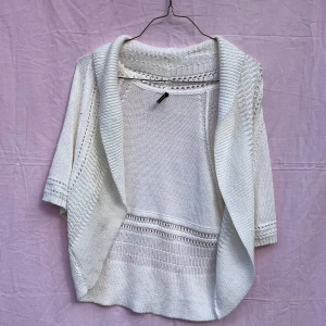Vit stickad kofta från Soyaconcept - Säljer en vit stickad kofta från Soyaconcept med korta ärmar och öppen front. Koftan har snygga ribbade detaljer och hålmönster längs kanterna och ärmsluten. Perfekt att slänga över en topp för en chill look. Fråga gärna om mått eller fler bilder!