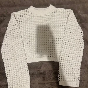 Vit croppad tröja, med hål - Säljer en vit croppad stickad tröja från H&M i storlek S. Tröjan har ett coolt hålmönster över hela och ribbad rund hals. Långärmad och perfekt för lager-på-lager. Passar dig som gillar trendiga och unika plagg. Knappast använd!
