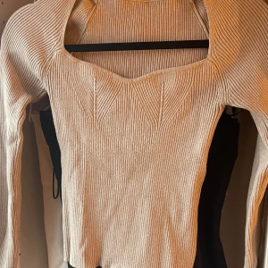 Beige ribbad långärmad topp - Supersnygg beige ribbad topp med lång ärm och unik fyrkantig urringning. Toppen har markerade sömmar framtill som ger en cool struktur och sitter tajt mot kroppen. Perfekt att styla med jeans eller kjol för en trendig look.