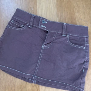 Brun minikjol - Så fin & slutsåld brun minikjol från HM med kontrasterande vita sömmar. Så fint jeansliknande tyg med fickor fram och bak samt bälteshällor.