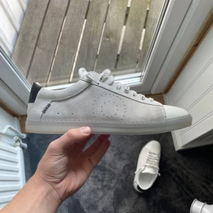 Vita sneakers från Oliver Cabell strl 40 - Snygga oanvända vita sneakers från Oliver Cabell (Sea Salt Ghost) i storlek 40. Ordinarie pris går på 250€ + frakt ca 30€ + tull 50€. Skorna har klassisk låg profil, rund tå och platt sula. Tillverkade i skinn med svarta detaljer på hälen och perforeringar på sidan. Tjocka vita snören med logga ger en clean och modern vibe. 