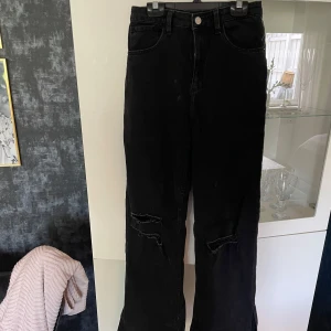 Svarta wide jeans från H&M - Säljer ett par svarta wide jeans från H&M med hög midja och justerbar midja. Jeansen har slitna detaljer vid knäna och slits vid benslut. Tillverkade i klassisk denim med en cool, loose passform. Helt oanvända! 