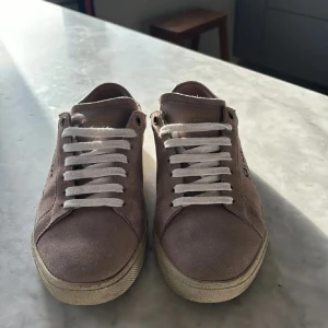 Saint Laurent beige mockasneakers - Snygga sneakers från Saint Laurent i beige mocka med vit sula och vita snören. Klassisk låg modell med rund tå och diskret logga på sidan. Perfekta för dig som vill ha en clean och stilren look med lyxig känsla.Köpta på plick, skriv till min om du har nån fråga, priset är inte hugget i sten! Storlek 39 men passar ungefär 39-40