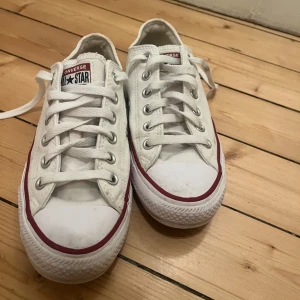 Vita låga converse - Klassiska vita Converse All Star sneakers med lågt skaft. Skorna har vit canvas, vita snören och en röd rand längs sulan. Används aldrig (vilket är anledningen till att jag säljer) och har bara används fåtal gånger.