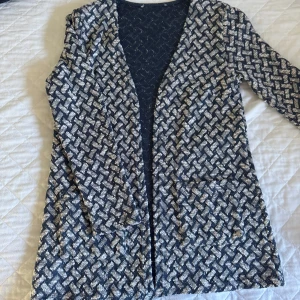 Mönstrad cardigan jacka i blått och vitt - Snygg cardigan jacka i blått och vitt med rutigt mönster. Jackan har lång ärm, öppen framtill och två praktiska fickor. Perfekt för lager-på-lager och ger en cool touch till din outfit.