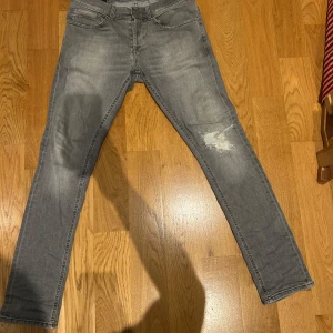 Dondup jeans  - Säljer ett par grå jeans från Dondup i storlek 31. De har en snygg slitning på ena knät och klassisk femficksdesign. Jeansen har rak passform och är tillverkade i mjukt denimtyg som är skönt att bära. Perfekt för dig som gillar en avslappnad och cool stil.