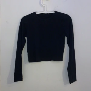 Svart croppad långärmad topp Stradivarius - En svart, enkel och croppad långärmad topp från Stradivarius. Modellen har rund halsringning och är figurnära i passformen. Perfekt att matcha med höga jeans eller kjol för en clean girl look. Pris kan diskuteras. 