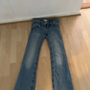Ljusblå bootcut jeans - Säljer ett par ljusblå jeans med bootcut-modell och snygg slitning på benen. Jeansen har låg midja, klassiska fem fickor och stängs med dragkedja och knapp. Perfekta för dig som gillar en retro vibe och vill ha ett par jeans med lite extra attityd. Köptes för 450 och i storlek 146-152