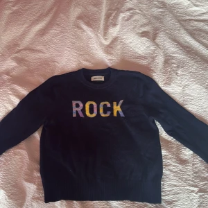 Mörkblå ull tröja Zadig & Voltaire - Snygg mörkblå ull tröja från Zadig & Voltaire med färgglad text 'ROCK' framtill. Tröjan har rund halsringning, långa ärmar och ribbade muddar. Perfekt för dig som vill ha en cool och bekväm look med lite edge.🐳🐳🏄🏼‍♀️🏄🏼‍♀️❤️❤️🌺