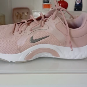 Nike rosa sneakers strl 39 - Nike sneakers i ljusrosa med silvrig swoosh och vita detaljer. Skorna har mesh-ovandel för bra ventilation, snörning och en mjuk, dämpad sula med Comfort Footbed. Snygg sportig look och passar perfekt för dig som gillar stilrena träningsskor. Använda 1 gång. Som nya❤️ Köpte dom för 739kr säljer dom för 200