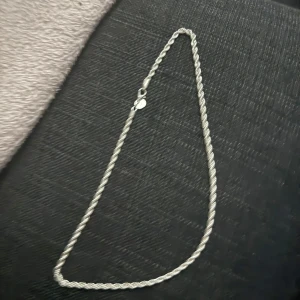 925 silver vriden halskedja - Säljer en snygg halskedja i äkta 925 silver med vriden design som ger en cool och modern look. Kedjan har en rund bricka vid låset där det står 925, vilket visar att den är gjord av sterlingsilver. Perfekt för dig som gillar stilrena smycken.