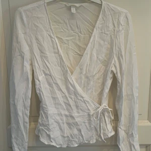 Vit omlottblus från H&M - Säljer en vit omlottblus från H&M🥰🥰Tröjan har ett litet spänne framtill som gör att man både kan ha den som första bilden men även som andra bilden!!🫶🏼🫶🏼