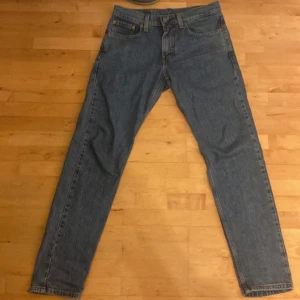 Levi's 502 blå jeansbyxor W28 - Klassiska blå Levi's 502 jeans med rak passform och normal midja. Byxorna har fem fickor, dragkedjegylf och tydliga Levi's-detaljer som röd etikett och läderpatch bak. Perfekta för dig som gillar tidlös denimstil.