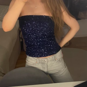 Mörkblå paljett-tubtopp - Säljer en glittrig mörkblå tubtopp täckt av paljetter. Perfekt för dig som vill sticka ut med en snygg och trendig topp. Toppen är ärmlös och har en tight passform som framhäver figuren.
