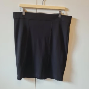 Pennkjol från Åhléns strl 46 - Klassisk svart pennkjol från Åhléns med hög midja och stilren design. Kjolen är tillverkad i en mjuk och stretchig mix av viskos, polyamid och elastan. Kjolens längd 54cm. Storlek 46. Kan hämtas i Vallentuna.