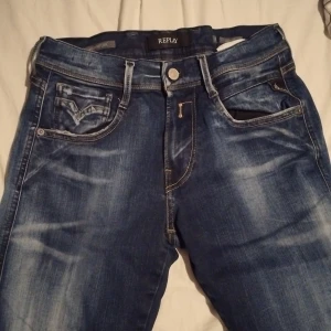 Blå Replay jeansbyxor herr - Säljer ett par klassiska blå jeans från Replay med snygga slitningar och detaljerade sömmar. Byxorna har normal passform, dragkedja och knapp framtill samt fem fickor. Perfekta för dig som gillar en tidlös jeanslook.