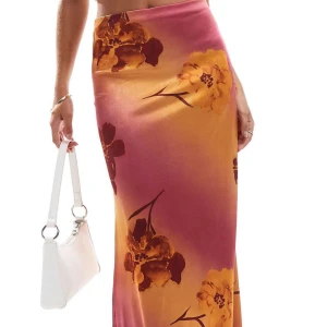 Lång blommig kjol  - Säljer en långkjol i satin med stora blommor i gula och bruna nyanser mot en rosa-orange bakgrund. Kjolen har en figurnära passform och hög midja, perfekt för sommaren. Säljer den då den inte passade mig så bra, helt oanvänd, nypris 369kr