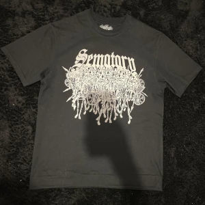 Sematary skellingtons shirt - Cool svart t-shirt med stort vitt tryck framtill med texten 'Sematary' och detaljerad grafik. På baksidan finns ett tryck av ett spöklikt träd och texten 'Haunted Mound'. Perfekt för dig som gillar unika och edgy plagg.