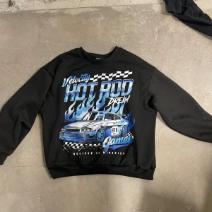Svart sweatshirt med biltryck från SHEIN - Cool svart sweatshirt från SHEIN med stort tryck av en sportbil, blåa flames och texten 'HOT ROD DREAM'. Tröjan har rund hals och långa ärmar. Perfekt för dig som gillar streetstyle och bilar.