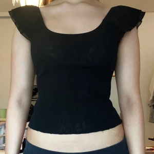Svart croppad mesh topp volangärm Vero Moda - Säljer en svart croppad topp från Vero Moda med volangärmar och rundad urringning. En äldre modell av vero moda. Köpt second hand. Lite sliten eftersom det är mesh material.