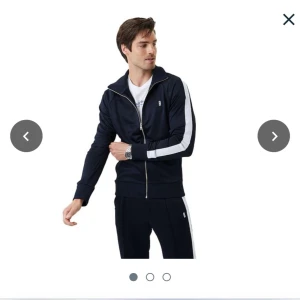 Svart träningsjacka från Björn Borg - Säljer en svart träningsjacka från Björn Borg med vit rand längs ärmarna och dragkedja framtill. Jackan har hög krage och ribbade muddar. Liten B-logga på bröstet och 'BORG' tryckt på ryggen. Perfekt för sport eller chill.