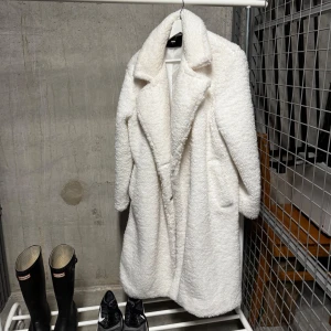 Vit teddyjacka från Bikbok - Säljer en fluffig och trendig vit teddyjacka från Bikbok. Jackan är lång med stora slag och har en mysig, mjuk känsla. Perfekt för att hålla värmen under kyliga dagar och ger en cool look till din outfit.