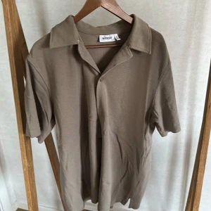 Beige kortärmad skjorta från Weekday - Säljer en  beige skjorta från Weekday med korta ärmar och klassisk krage. Skjortan har en avslappnad passform.
