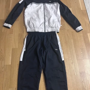 Lacoste dress - Säljer en stilren Lacostedress i prasligt tyg perfekt till våren. Jackan ör använd 2-3 gånger då den va flr liten och byxorna ör aldrig använda. Byxorna ör i en storlek större. Byxorna är i L och jackan M. Hör av er vid funderingar. 