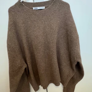 Brun stickad tröja från Zara - Mysig brun stickad tröja från Zara med rund halsringning och avslappnad passform. Perfekt för kyliga dagar och enkel att matcha med olika outfits. Ribbstickade muddar vid ärmslut och nederkant.