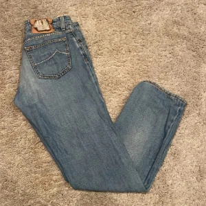 Blå jeansbyxor från Jacob Cohen - Säljer ett par klassiska blå jeans från Jacob Cohen med fem fickor och snygga kontrastsömmar. Byxorna har normal passform och är tillverkade i mjukt denimtyg. Perfekta till vardags för en avslappnad stil.