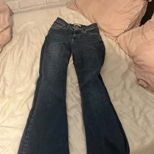 Blå bootcut jeans - Säljer ett par klassiska blå bootcut jeans med normal passform. Jeansen har fem fickor, knapp- och dragkedjegylf samt breda benslut. Perfekta för dig som gillar en retroinspirerad look.