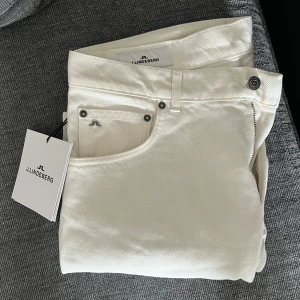 Vita jeansbyxor från J.Lindeberg - Snygga vita jeansbyxor från J.Lindeberg med klassisk femficksdesign och silverfärgade nitar. Byxorna har raka ben och normal passform. Perfekta för en stilren look och lätta att matcha med olika outfits., Har fått som julklapp men inte använt då storlek ej passar, Byxan är Storlek 34/32 Nypris ligger på 1300kr se mindre