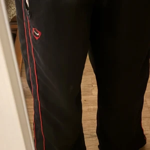Svarta mjukisbyxor med röd detaljsöm - Nike träningsbyxor i bra skick. Väldigt sköna k material och passar bra. De har snören som ändrar passar formen till det du vill ha.  Hör av dig för frågor💕